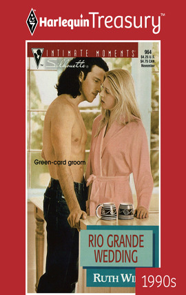 A shirtless man in dark jeans with shoulder-length, dark brown hair leans in towards a blonde woman wearing a pink bathrobe. They're in a sunny kitchen, standing next to a counter that has two coffee cups on it.